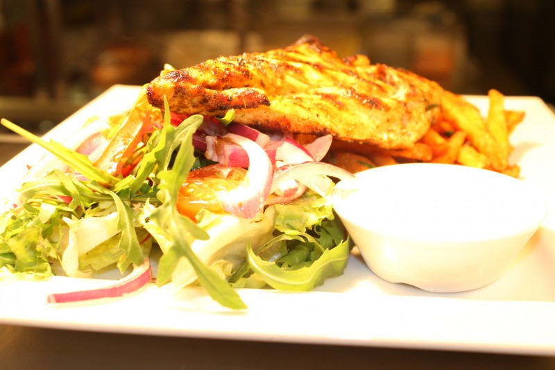 Plate of grilled meat with salad greens, red onion, fries and a small white sauce bowl, warm lighting