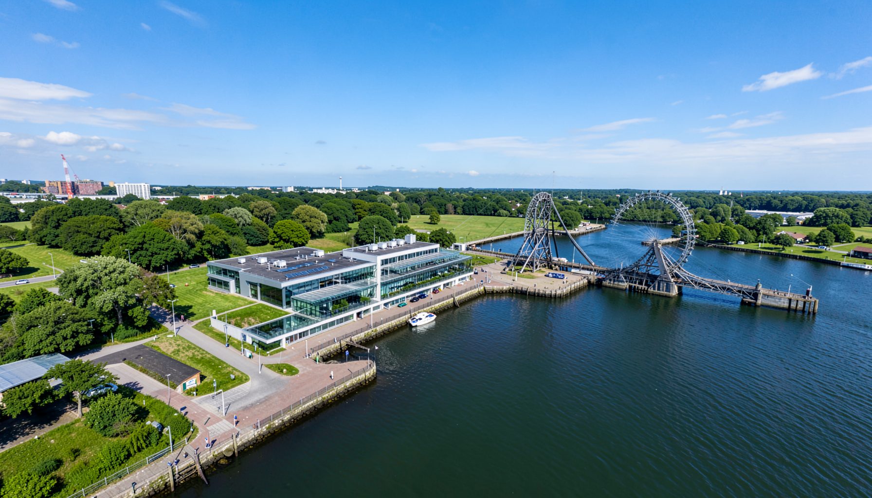 Aerial view of a waterfront area with a modern building near the Falkirk Wheel, green surroundings and blue sky