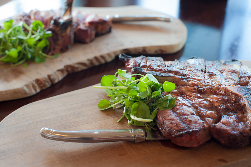 Close-up of grilled steak slices garnished with fresh greens on wooden boards, warm brown and green tones, appetizing food presentation